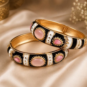 May include: Two gold-tone hinged bangle bracelets featuring alternating black and white enamel sections. The bracelets are decorated with oval and teardrop-shaped pink cabochon stones set within gold-tone scalloped frames and small gold beads.
