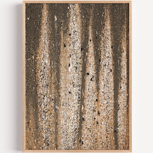 Könnte beinhalten: Ein gerahmter vertikaler Wandkunstdruck mit einer hochauflösenden Nahaufnahme von nassem Sand an einem Strand. Das Bild zeigt abwechselnde vertikale Bänder aus dunklem, feuchtem Sand und helleren, texturierten Sandbereichen mit kleinen Kieselsteinen.
