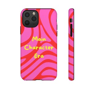 Könnte beinhalten: Eine Smartphone-Hülle mit einem leuchtend pinken und roten wellenförmigen Wirbelmuster. Der Text "Main Character Era" ist in Gelb in der Mitte aufgedruckt. Die Hülle hat einen schwarzen Kameraausschnitt und schwarze Seitentasten.