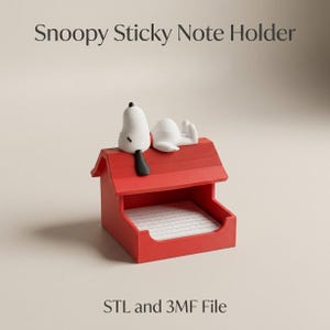Può includere: Un portablocco per note adesive a forma di cuccia rossa con una figura bianca di Snoopy dalle orecchie nere sdraiata sul tetto. Il testo "Snoopy Sticky Note Holder" appare sopra e "STL and 3MF File" è stampato sotto la struttura rossa.