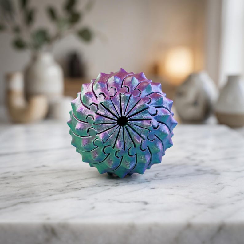 May include: A spherical object with a complex, interlocking geometric pattern featuring a metallic, iridescent finish that shifts between shades of purple, blue, and green. The structure has a central circular opening and a textured, repeating design.
