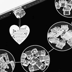 May include: A heart-shaped pendant with the word "Mum" and a message, hanging from a clear plastic object. The image also shows several clear earring backs in circular arrangements, with a black background.