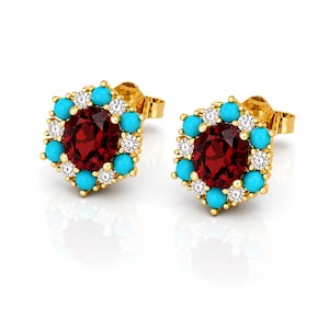 May include: A pair of gold stud earrings. Each earring features a central, round, deep red gemstone surrounded by turquoise and small white gemstones. The earrings have a hexagonal design.