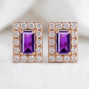 May include: A pair of rectangular stud earrings set in rose gold. Each earring features a central emerald-cut purple amethyst gemstone surrounded by a halo of small, round, clear white diamonds or cubic zirconia stones in a classic frame.