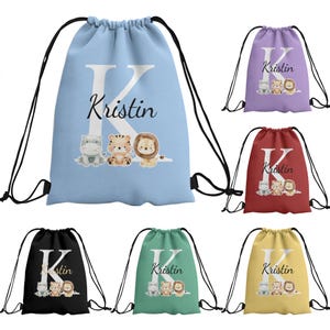 Può includere: Una collezione di sei zaini con coulisse in azzurro, viola, rosso, nero, verde e giallo. Ogni borsa presenta una grande lettera K bianca, il nome Kristin in corsivo nero e una grafica con un ippopotamo, una tigre e un leone.