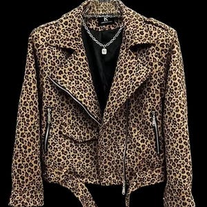 May include: A brown and tan leopard print jacket with a black interior. The jacket has a zip closure, side pockets, and a belt. A silver necklace with a pendant is visible. The jacket is hanging on a black hanger.
