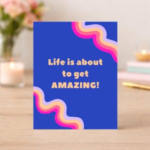 Puede incluir: Tarjeta de felicitación azul con el texto "Life is about to get AMAZING!". Presenta diseños ondulados y coloridos en rosa, naranja, amarillo y morado. Ideal para enviar a un ser querido.