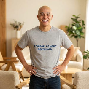 Puede incluir: Una camiseta gris con el texto "I Speak Fluent Metadata" en azul. La camiseta de manga corta la lleva una persona sonriendo, con las manos en las caderas.