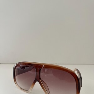 May include: Brown oversized sunglasses with a gradient lens. The sunglasses have a thick frame and a classic aviator shape. The lenses transition from a light brown to a darker brown. The sunglasses are a stylish accessory.