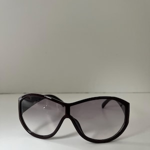 Pu&ograve; includere: Occhiali da sole oversize marrone scuro con lenti sfumate. Gli occhiali hanno una montatura spessa e una forma arrotondata, che offre un look audace ed elegante. Le lenti passano da scure nella parte superiore a pi&ugrave; chiare nella parte inferiore.