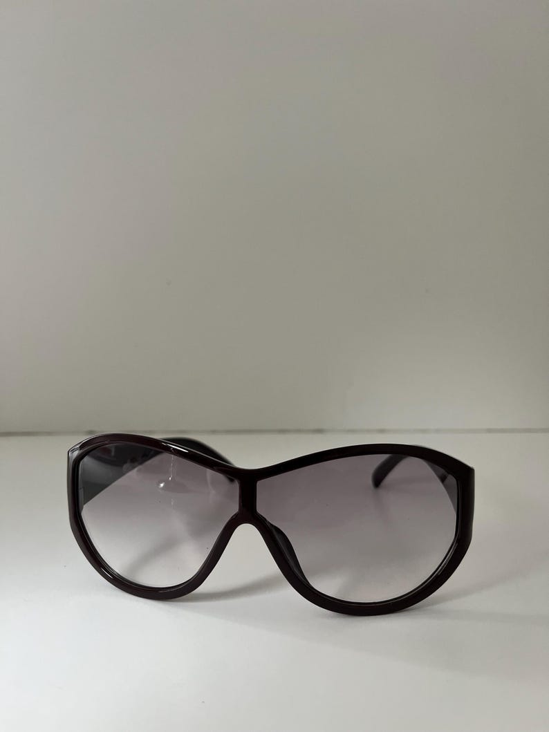Pu&ograve; includere: Occhiali da sole oversize marrone scuro con lenti sfumate. Gli occhiali hanno una montatura spessa e una forma arrotondata, che offre un look audace ed elegante. Le lenti passano da scure nella parte superiore a pi&ugrave; chiare nella parte inferiore.