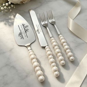 May include: A silver cake serving set comprising a cake server, a knife, and two forks. Each piece features handles made of white faux pearls. The server and knife are engraved with the text Benjamin & Charlotte 05.20.2025 and leaf motifs.