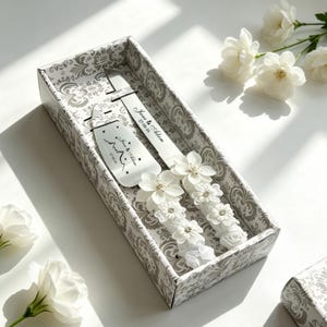 May include: A wedding cake knife and server set in a decorative box. The set includes a knife and server with white floral accents and the names "Jane & Adam" and the date "27-08-26" printed on them. The box has a gray and white damask pattern.