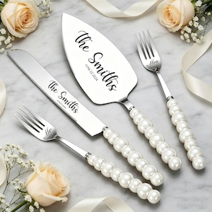 May include: A wedding cake serving set with a cake knife, server, and two forks. The stainless steel utensils have pearl-like handles and are engraved with "The Smiths" and the wedding date. The set is displayed with flowers.