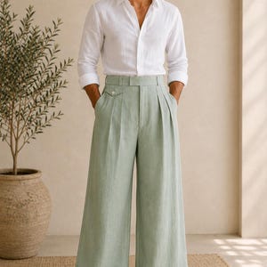 May include: A white long-sleeved button-down shirt paired with high-waisted, wide-leg trousers in a pale sage green color. The trousers feature double pleats at the waist, a small buttoned coin pocket detail, and wide cuffs at the hem. The text ZAYRO TAILOR is visible.