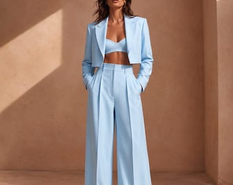 May include: A light blue three-piece set consisting of a cropped blazer with notched lapels, a matching sweetheart neckline bralette, and high-waisted wide-leg trousers with front pleats and side pockets, all in a solid pastel blue fabric.