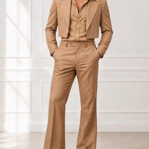 Può includere: Un completo color marrone chiaro composto da un blazer corto con ampi revers, una camicia abbottonata coordinata e pantaloni a zampa a vita alta. L'outfit è completato da scarpe eleganti in pelle marrone, creando un look monocromatico.