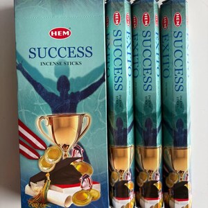 May include: A teal box and three teal cylindrical boxes of HEM Success incense sticks. The box features a silhouette of a person with arms raised, a gold trophy, graduation cap, and coins. The text "SUCCESS INCENSE STICKS" is displayed on the box.