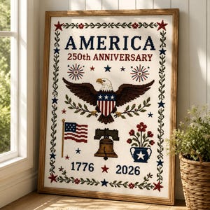 Op de afbeelding: Een ingelijste kruissteek met de tekst AMERICA 250th ANNIVERSARY 1776 2026. Het ontwerp bevat een centrale Amerikaanse zeearend met een schild, een Amerikaanse vlag, de Liberty Bell, een bloempot en sterren, omringd door een bloemenrand.