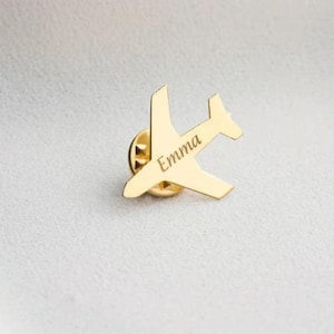 以下が含まれることがあります： 側面 に「Emma」と刻印された、金色の飛行機のピン。 このピンは、翼と尾を持つ飛行機の小さな詳細な表現です。 このピンは、衣類やアクセサリーに取り付けるように設計されています。
