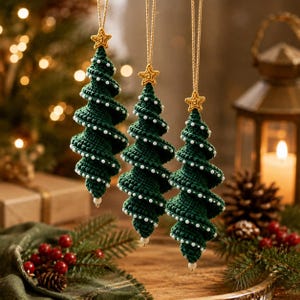 Könnte beinhalten: Drei spiralförmige Weihnachtsbaumschmuckstücke aus dunkelgrünem Häkelgarn. Jeder Baum ist an der Spitze mit einem kleinen goldfarbenen Stern versehen und entlang der spiralförmigen Kanten mit winzigen weißen Perlen verziert. Jeder Anhänger hängt an einer beigen Schnur.