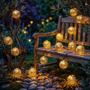 May include: A string of spherical, gold-toned metal lanterns featuring intricate cut-out patterns that emit a warm, glowing light. The decorative lights are draped across a wooden bench and a metal garden structure, creating a soft illumination.