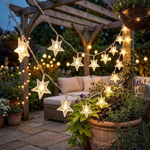 May include: A string of LED fairy lights featuring clear, five-pointed star-shaped covers. The lights are draped across a wooden pergola, emitting a warm glow. Each star contains a small bulb, creating a decorative illumination for outdoor spaces.