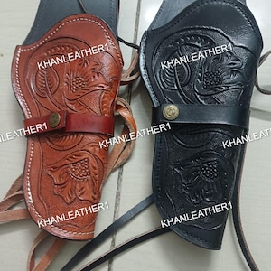 Op de afbeelding: Twee lederen holsters, één in lichtbruin en één in zwart, met gedetailleerde florale patronen. Elk holster heeft een horizontale riem die is vastgezet met een messingkleurige metalen drukknoop. De tekst KHANLEATHER1 is zichtbaar op de items.