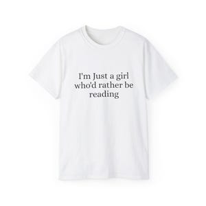 May include: White t-shirt with the text "I'm Just a girl who'd rather be reading" in black. The shirt has a crew neck and short sleeves. The text is centered on the front of the shirt.