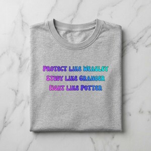 May include: A folded gray t-shirt with the text "PROTECT LIKE WEASLEY, STUDY LIKE GRANGER, FIGHT LIKE POTTER" in a gradient of blue, purple, and green. The shirt is on a white and gray marble surface.