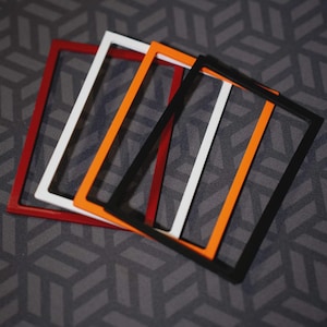 May include: A set of four rectangular frames in red, white, orange, and black. Each frame features a thin, flat border with an open center, arranged in a slightly overlapping, staggered formation to display the distinct solid colors of each piece.