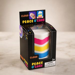 May include: A cylindrical cake-shaped toy inside a black cardboard box labeled Cloud Peace O'Cake. The toy features horizontal stripes of white, pink, yellow, and blue. The packaging includes colorful sprinkles, a warning label, and age rating 3+.