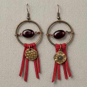 Op de afbeelding: Een paar handgemaakte oorbellen met messing hoepels, donkerrode kralen en rode suède franjes. Elke oorbel heeft een gehamerde messing schijf hanger. De oorbellen hebben een bohemien of tribaal design.