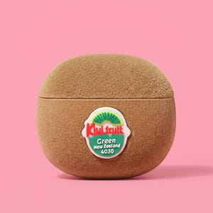 Puede incluir: Un recipiente marrón con forma de kiwi y superficie texturizada. El recipiente tiene una etiqueta blanca, verde y roja que dice "Kiwi fruit Green New Zealand 4030". El fondo es rosa.