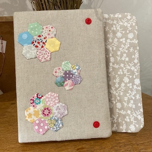 Puede incluir: Un tablero de notas de tela beige con tres diseños florales hechos de tela estampada colorida. Dos chinchetas rojas aseguran el tablero. Se ve un segundo tablero con un estampado floral.