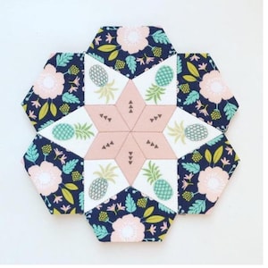 Peut inclure: Un dessous de verre en tissu fait à la main en forme d'étoile avec un motif floral et ananas. Le dessous de verre présente un fond bleu marine avec des fleurs roses et des feuilles vertes. Le centre a une étoile rose avec des accents d'ananas blancs et verts. Le dessous de verre mesure environ 15 cm de diamètre.