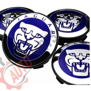 Könnte beinhalten: Vier Jaguar-Radnabenabdeckungen. Jede Kappe zeigt ein blau-silbernes Jaguar-Logo mit dem Wort "JAGUAR" in silbernen Buchstaben. Die Kappen haben einen schwarzen Sockel und eine glänzende, reflektierende Oberfläche.
