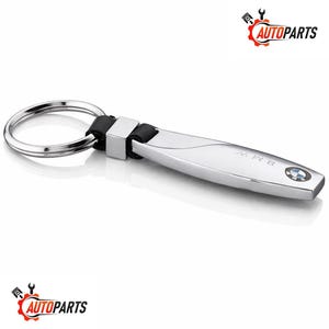May include: A silver BMW keyring with a black leather strap and a metal ring. The keyring has the BMW logo and the word "BMW" engraved on it. The keyring is a car accessory.