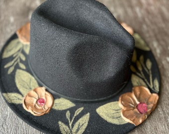 May include: A black fedora hat with a wide brim decorated with gold and brown floral designs.