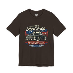 May include: A dark brown t-shirt featuring a graphic of a vintage black Ford F-100 pickup truck. The design includes the text "1953 Ford F-100" above the truck and "Truck Heritage Driven with Pride" below, with red, white, and blue accents.