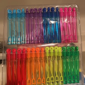 May include: A clear plastic package filled with colorful bubble wands. The wands are arranged in rows, with each row featuring a different color, including blue, purple, pink, red, orange, yellow, and green. The wands are filled with bubble solution.