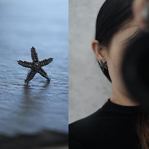 Op de afbeelding: Een zilveren zeester-oorbel en een bijpassende zeester-ring. De sieraden zijn gemaakt van kleine, ronde kralen. De oorbel wordt gedragen op het oor van een persoon. De zeester is een populair ontwerp met een oceaanthema.