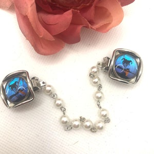 May include: A pair of silver tone butterfly wing jewellery clips connected by a chain of faux pearls.