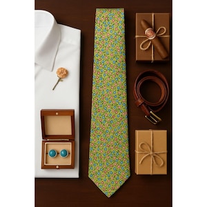 May include: An overhead shot of a white dress shirt, a green floral tie, a brown leather belt, a cigar, and a pair of turquoise cufflinks in a wooden box. The items are arranged on a dark brown surface.