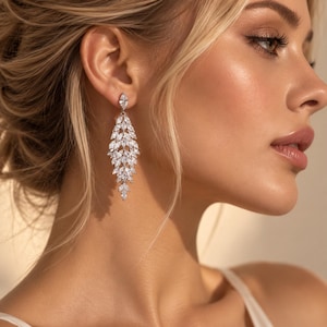 May include: A long, dangling earring featuring a silver-toned metal setting adorned with numerous clear, marquise-cut stones arranged in a cascading, leaf-like pattern that tapers towards the bottom, secured with a single marquise-cut stone stud.