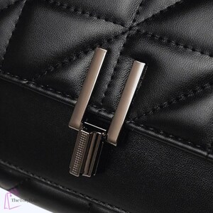 Puede incluir: Primer plano de un bolso de mano de cuero negro acolchado con un cierre plateado. El bolso presenta un patr&oacute;n de diamantes y un cierre met&aacute;lico rectangular. El cuero parece liso y las costuras son visibles.