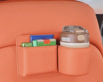 Pode incluir: Organizador de assento de carro laranja com porta-copos e bolso pequeno. O porta-copos contém uma caneca de viagem marrom e branca. O bolso contém caixas retangulares pequenas em verde, azul e laranja.