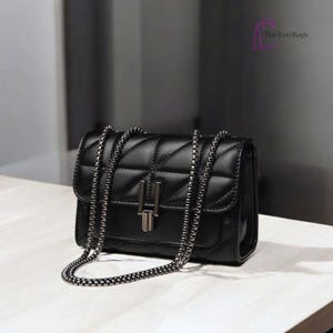 Puede incluir: Bolso bandolera negro acolchado con cadena plateada. El bolso tiene forma rectangular con cierre de solapa y cierre met&aacute;lico plateado. El logotipo de TotyBags est&aacute; en la esquina superior derecha.