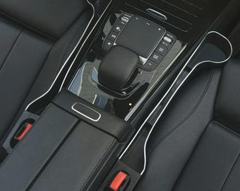 Pode incluir: Organizador de assento de carro preto com um design elegante. Possui um porta-copos e uma ranhura para armazenamento. O organizador tem uma moldura prateada e foi projetado para caber entre os assentos. O texto "Black" está no canto superior esquerdo.