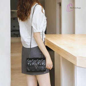 Puede incluir: Bolso bandolera negro acolchado con cadena plateada y cierre plateado. El bolso tiene forma rectangular y un patr&oacute;n de diamantes. El logotipo de The Toty Bags es visible.